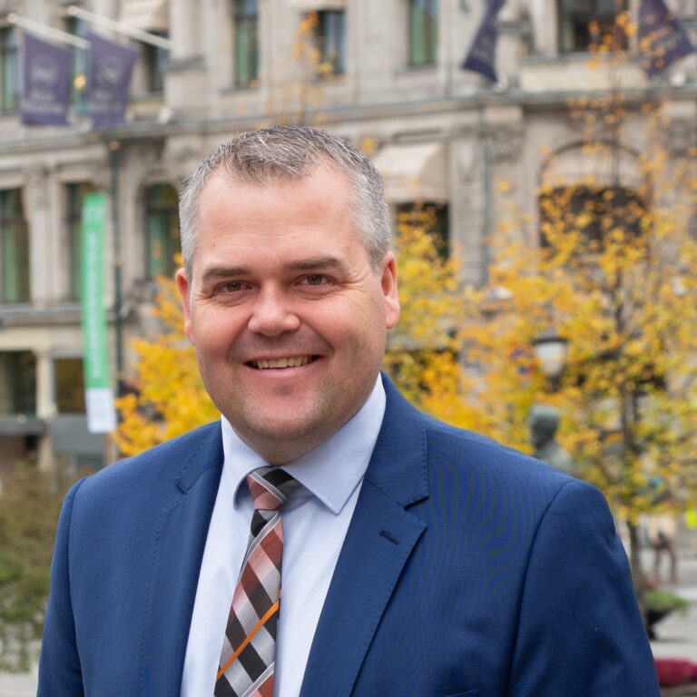 Roy Steffensen. Smilende utenfor Stortinget, trær i høstfarger i bakgrunnen. Portrett. Foto.