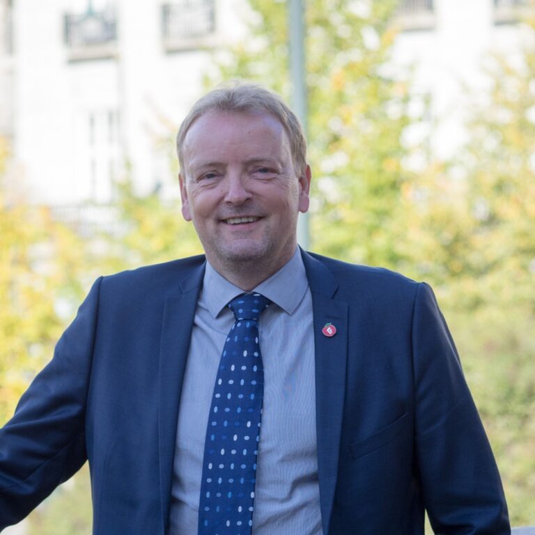 Terje Halleland smilende foran grønne trær. Portrett. Foto