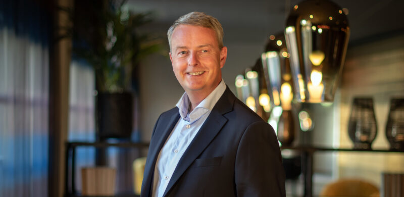 Terje Søviknes, smilende i mørk dress. Uskarp bakgrunn. Portrett. Foto.